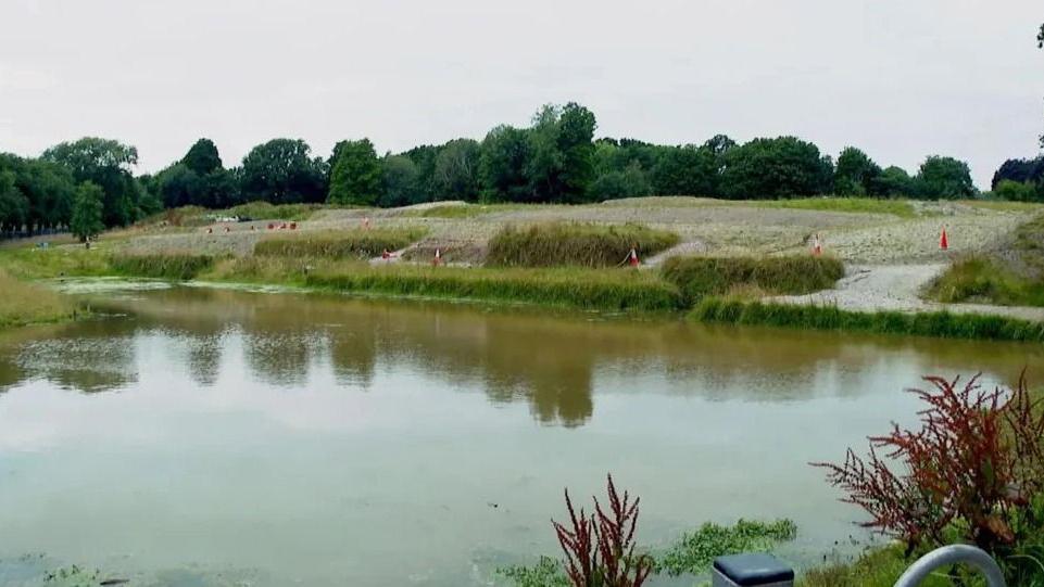 Wide shot of a pond with traffic cones around the edges. The pond is lowered, with grass around the outside.