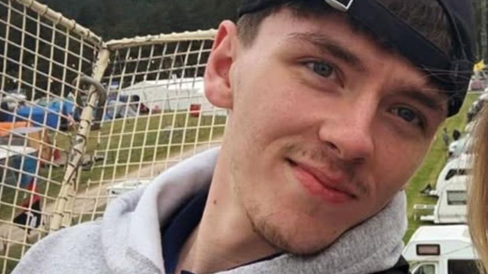 Ruben MacDonald is a young man with dark hair under a cap and designer stubble. He is pictured outdoors wearing a grey hooded top.