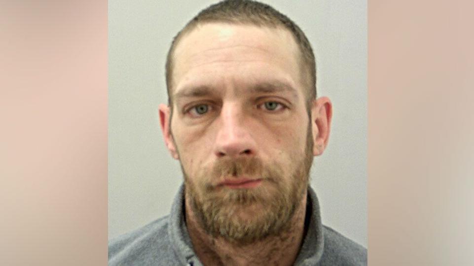 A police mugshot of Martin Crossley, who has short light brown hair and a brown beard