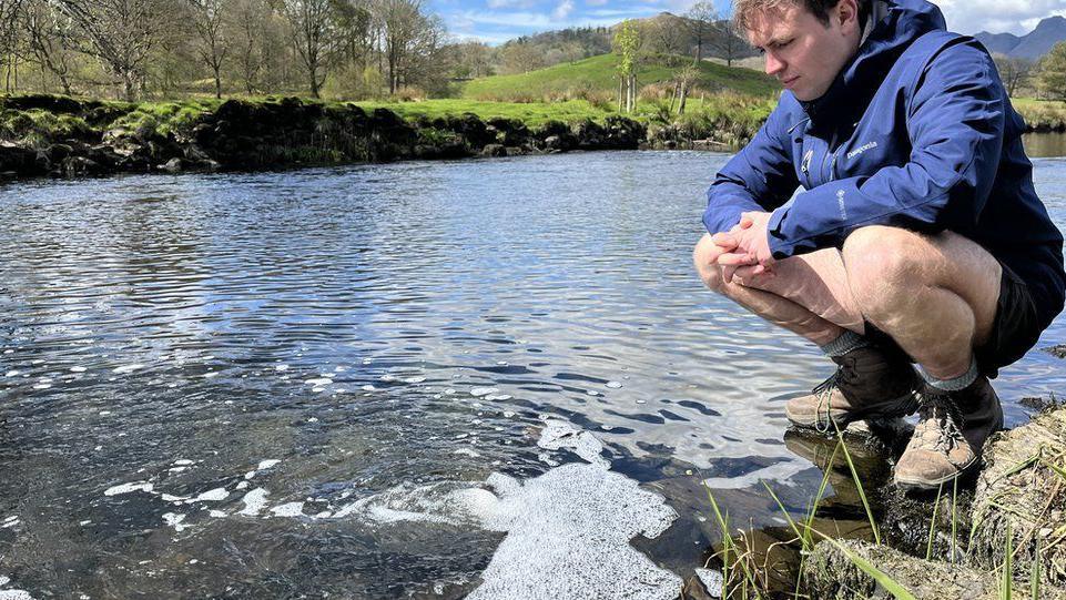 Matt Staniek crouched down on a rock looks into a stream