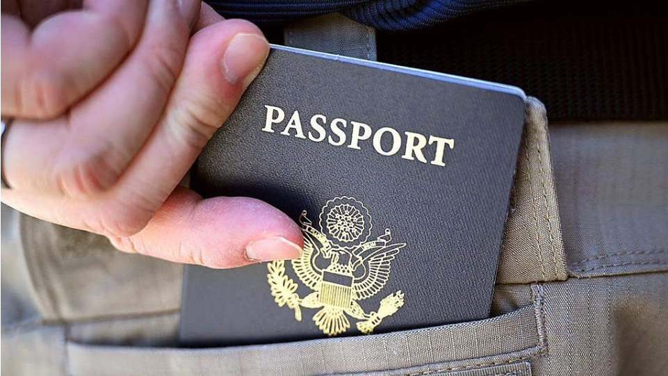 A person is seen with a US passport. Part of it is in a bag.