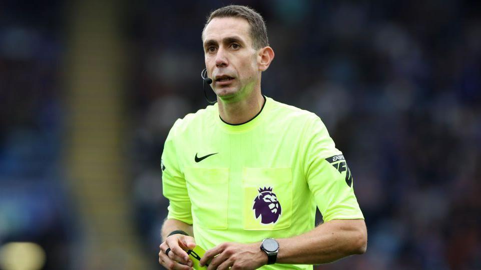 David Coote holds a yellow card during a Premier League match