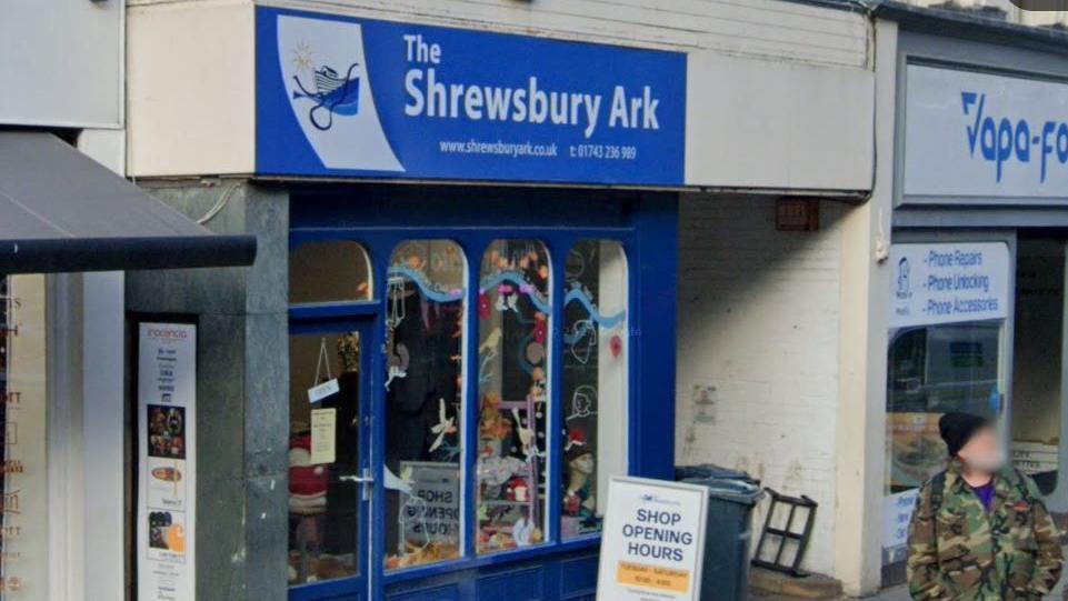 A shop with large glass windows and a blue painted front with the words The Shrewsbury Ark above the door