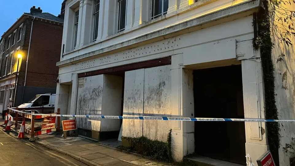 A large white derelict building with police tape in front of it