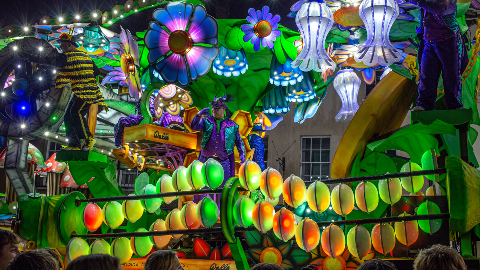 A stunning carnival float of neon green, yellow and blue flowers, garlands, leaves and men in purple suits. The Walls logo is visible on the float