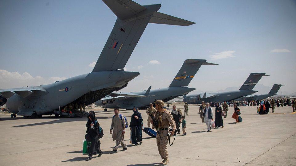 Members of the UK Armed Forces leading Afghan refugees past a row of RAF transport planes at Kabul airport. The refugees' faces have been blurred