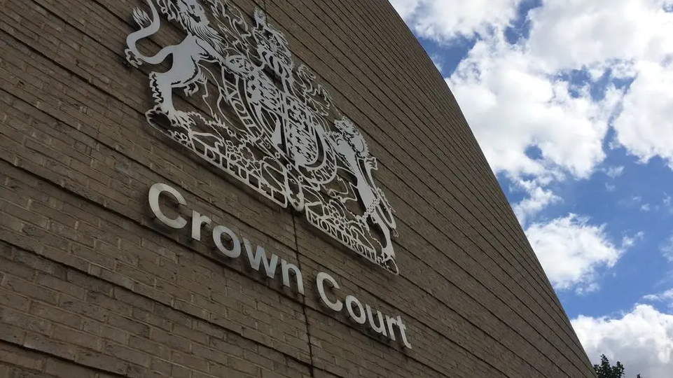 Exterior of Cambridge Crown Court, a rounded brick building with a risen view of the court crest against a summer sky