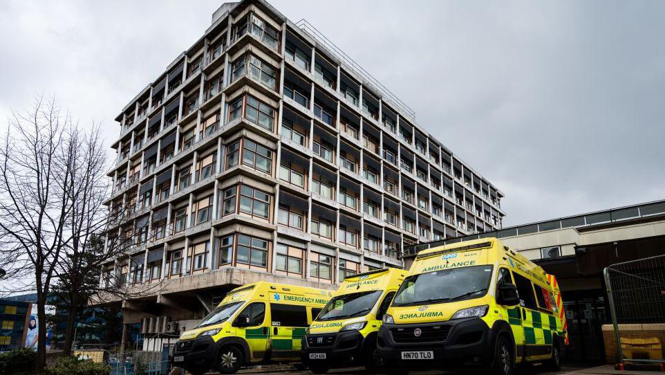 A eight-storey hospital tower block with three ambulances parked outside