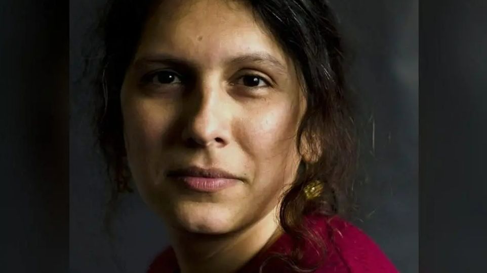 Mridul Wadhwa looking directly at the camera. She is wearing a dark coloured top and is in front of a dark background. She has a gold earring in her left ear.