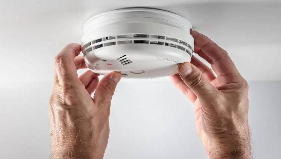 hands adjusting a smoke alarm on a ceiling