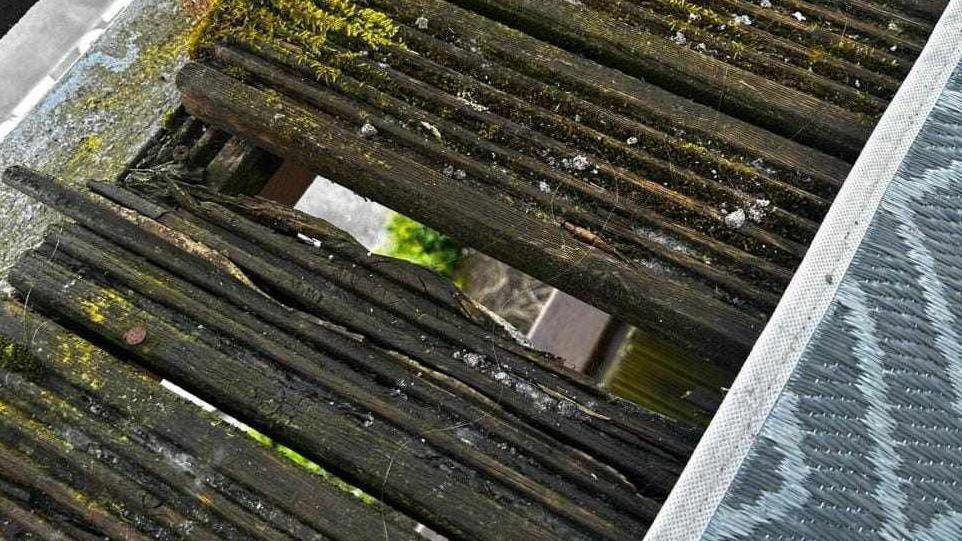 Rotten boards on a balcony. The floor below can be seen below through a gap in the slats. 