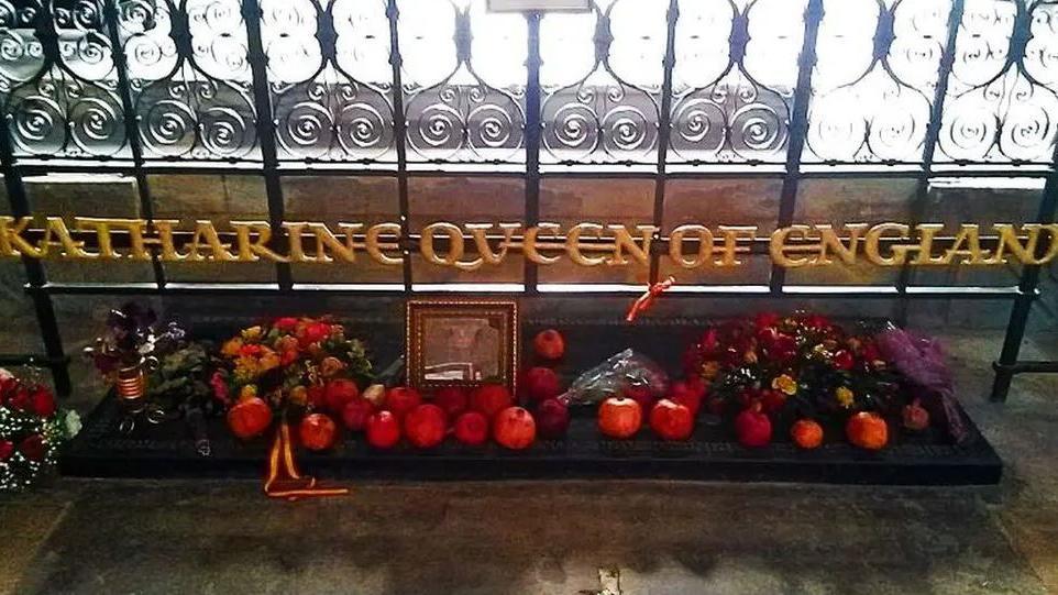 Katharine of Aragon's tomb. It has fruit, flowers and a picture in a frame laid on it, and gold lettering above it that reads: " Katharine Queen of England"