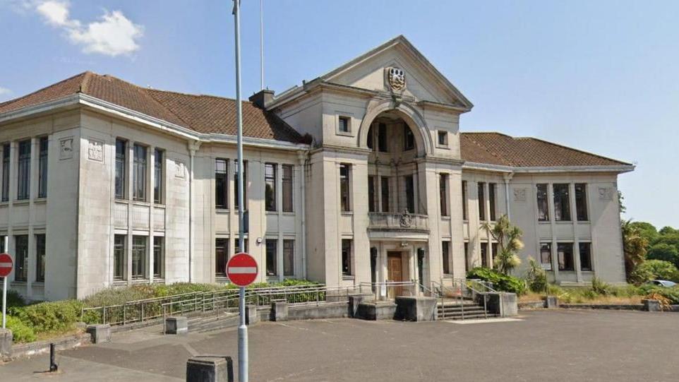 A Google Street View of Poole Civic Centre - a wide symmetrical Art Deco-style municipal building built of white stone with a pitched terracotta-coloured roof. Steps lead up to the central main door, above which is a large arch and a recessed balcony