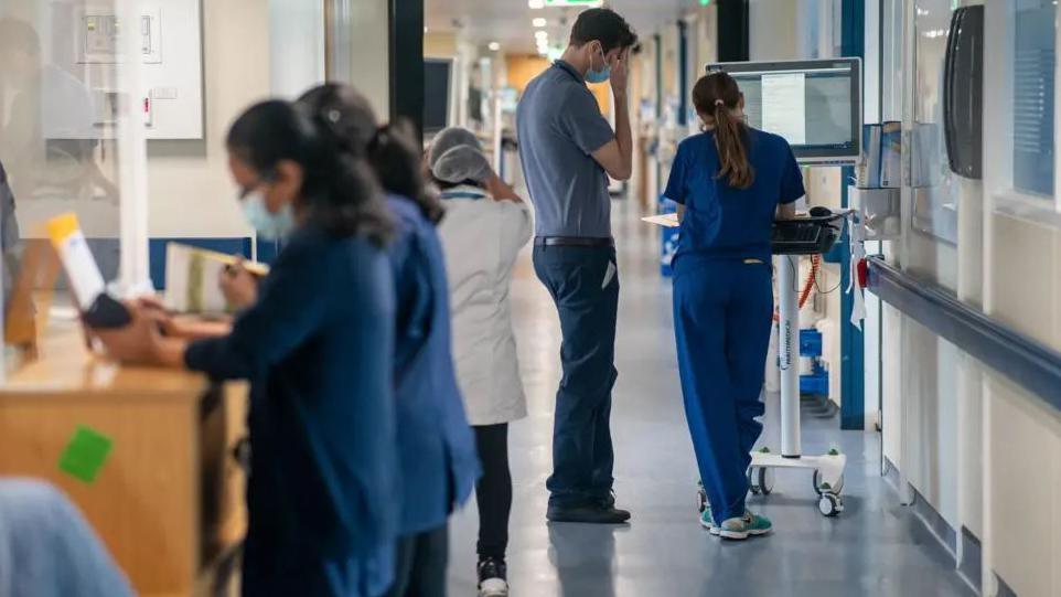 Doctors and nurses walking and standing in a busy hospital corridor.
