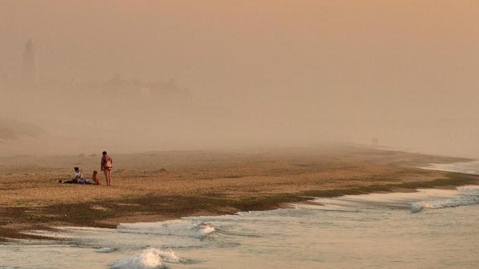 A photograph of Southwold beach showing people on a misty, windswept stretch of sand with the town's lighthouse just visible in the background


