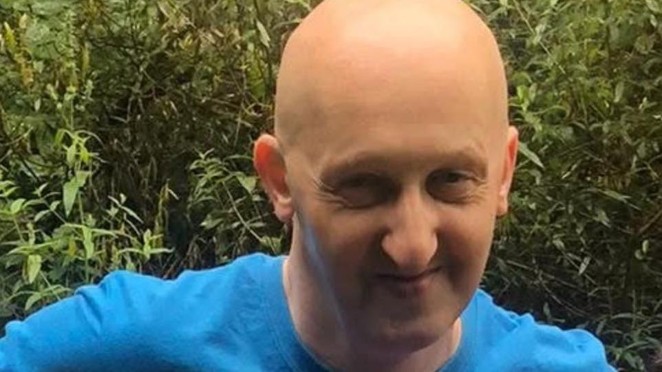 A picture of Adrian Daulby. Smiling, he is wearing a blue t-shirt and has a bald head.