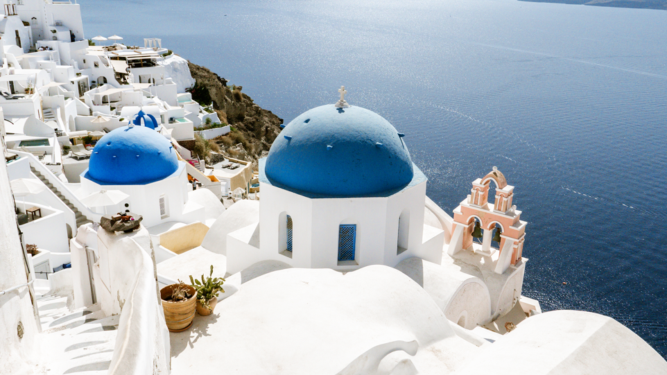 Beautiful white architecture in a village in Santorini, in Greece, with blue orb-like roofs. They overlook a vast landscape and ocean view.