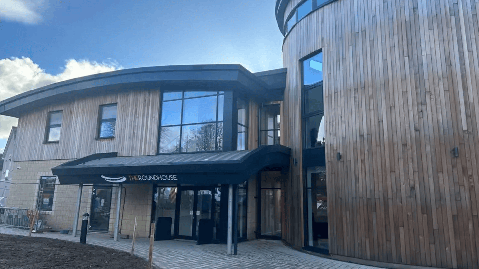 A two-storey modern building with a canopied lobby entrance with "The roundhouse" written over the top, and a glass, wood panel and concrete facade.