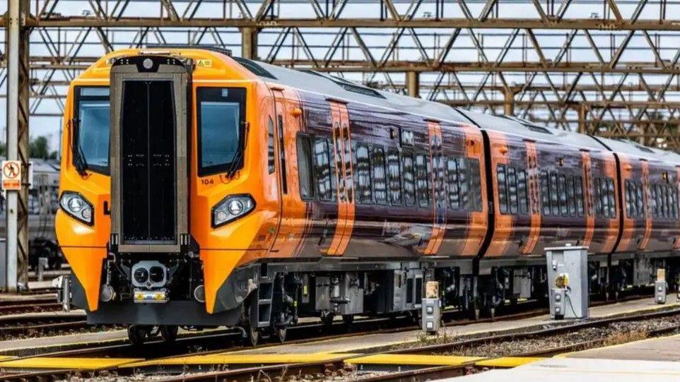 The outside of a West Midlands Railway train, which is painted orange and purple, standing on trains tracks.