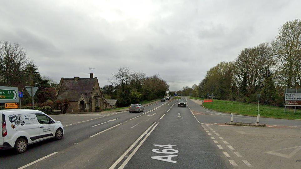 A64 crossroads between Scarborough/Malton and York, close to Crambeck Village. A white van in the foreground with other cars driving away from and towards the camera. A brown sign for Castle Howard to the left.