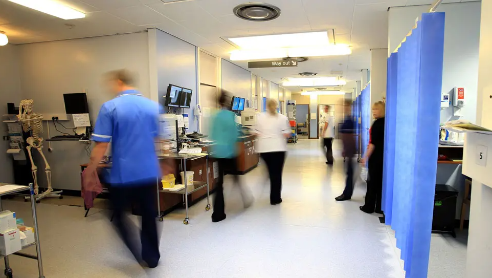 Busy hospital ward in action with gowned and uniformed staff moving around curtained areas and corridors