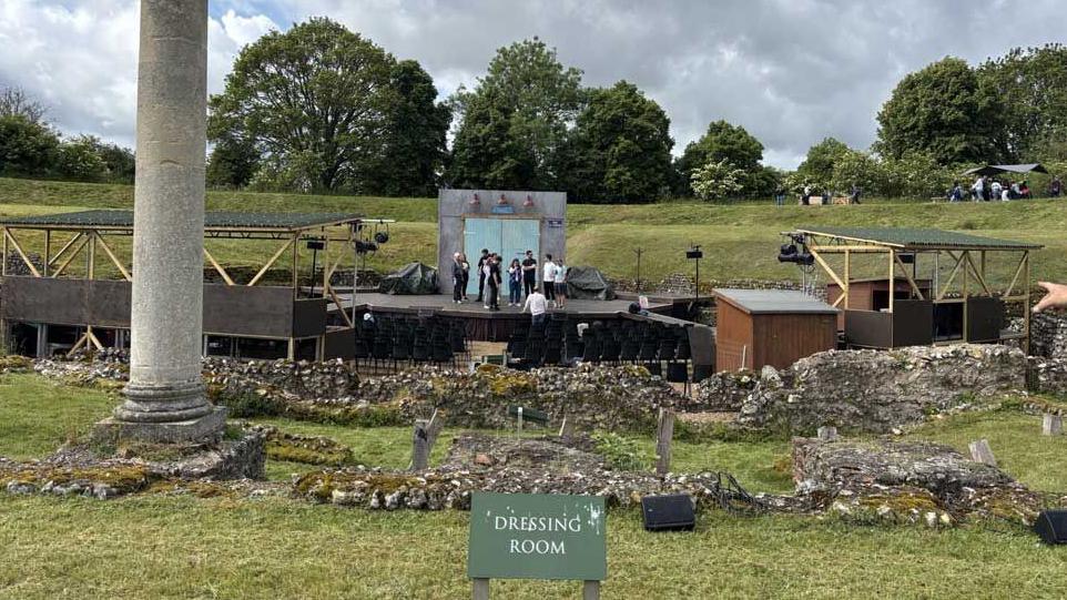 In the foreground are the ruins of the Roman dressing room, behind you can see modern seating and the position of the stage in the 21st century with actors rehearsing on it.