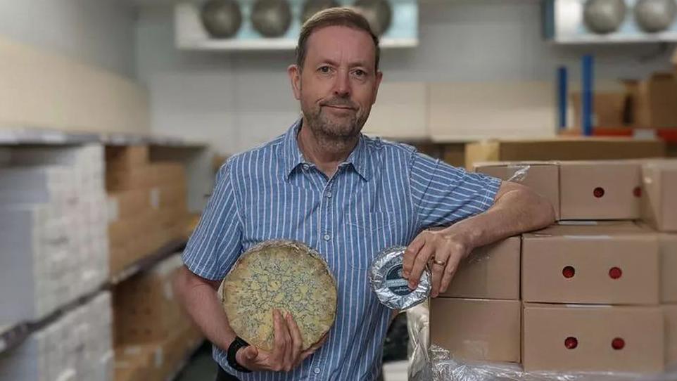 Simon Spurrell stood holding a wheel of blue cheese