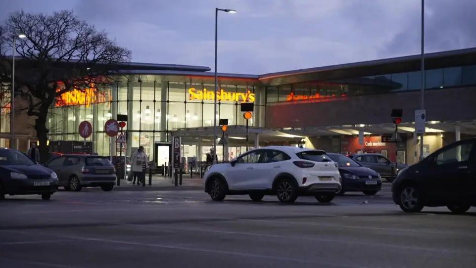 A car park outside a Sainsburys at a retail park on Wilsmlow Road