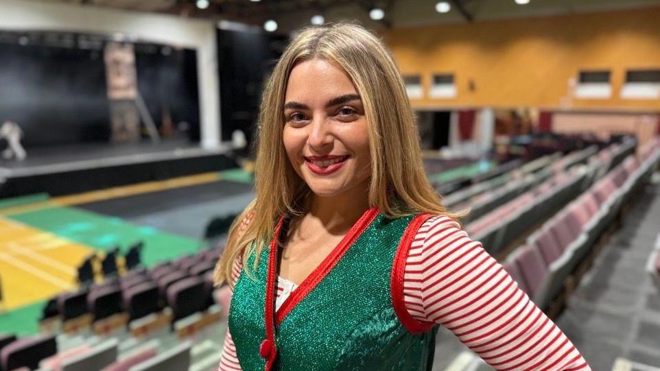 A smiling Jade MayJean looking straight at the camera. She is wearing a sparkly green waistcoat over a red and white striped long sleeved top.