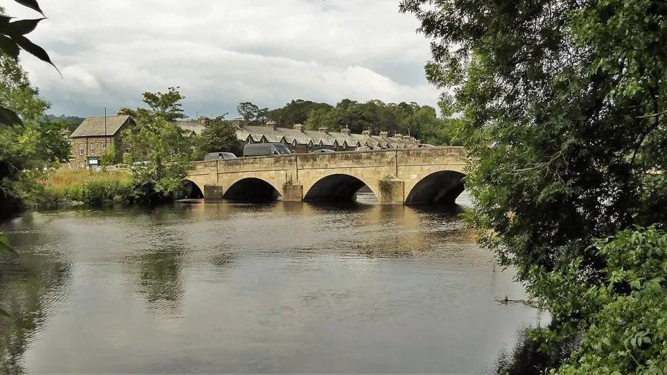 A bridge spanning a river, pictured from across the water. There are some trees to the side. 