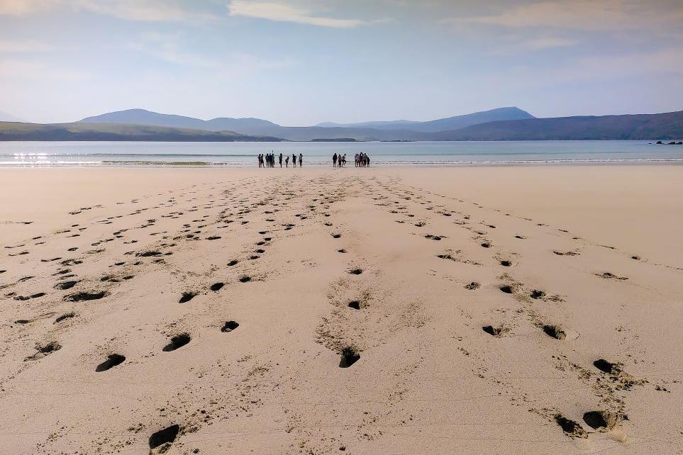 Footprints on a sandy beach and a group of people standing by the sea