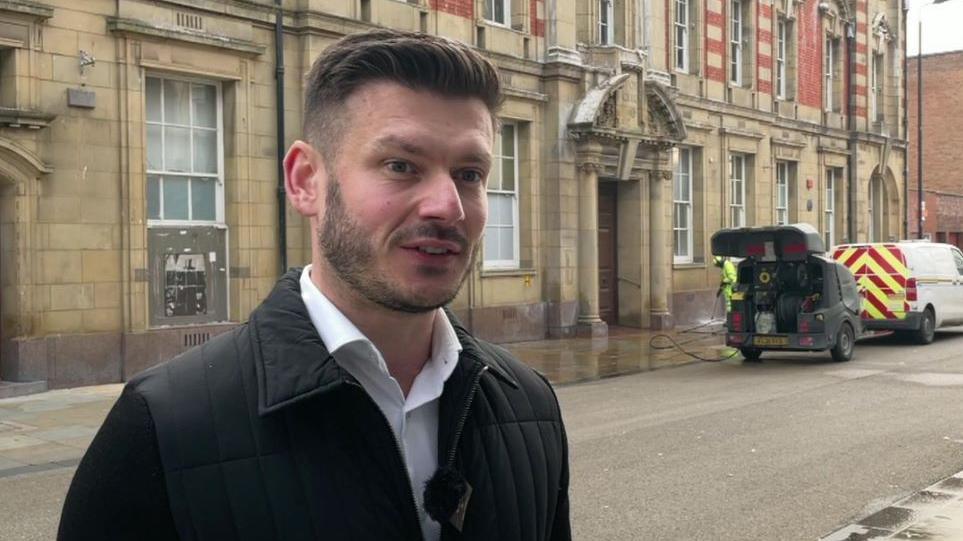 Keane Duncan standing in front of a man power washing the pavements to get rid of bird poo