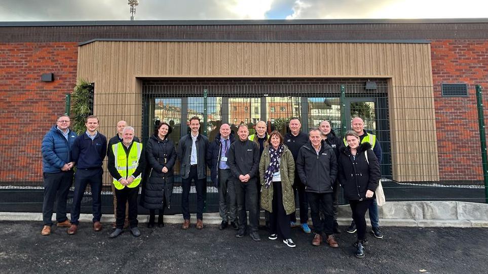 Warden Construction handing the keys over to Blackpool Council and Blackpool Boys and Girls Club outside the new youth centre, a large single storey red brick building with a wood framed glass entrance