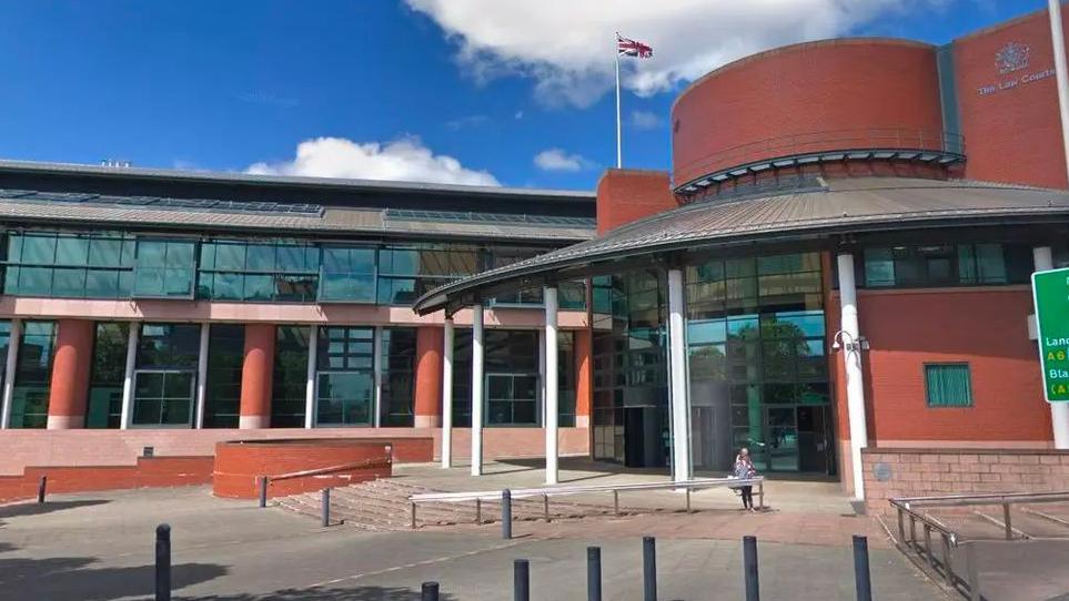 Street view image of Preston Crown Court, a glass and red brick building, with a round entrance