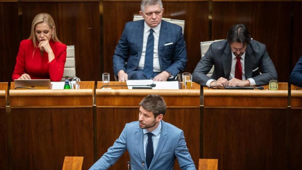 Slovakia's Prime Minister Robert Fico looks on as the leader of the opposition, wearing a light blue jacket and tie, addresses parliament in Bratislava