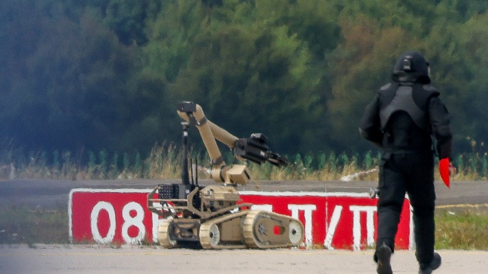 A police officer in dark protective clothing walks next to an explosive-disarming robot at Leipzig/Halle Airport on 5 August 2026