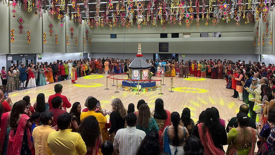 Hundreds of people stand on the edge of the room with the goddess shrine in the centre of the floor while the light wick ceremony takes place