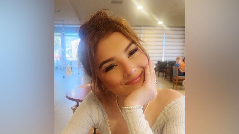 Demi-Leigh Davies smiling with her head to the side and chin resting on her hand. She is wearing a cream top and pearl bracelet and necklace and brown hair in a cafe.