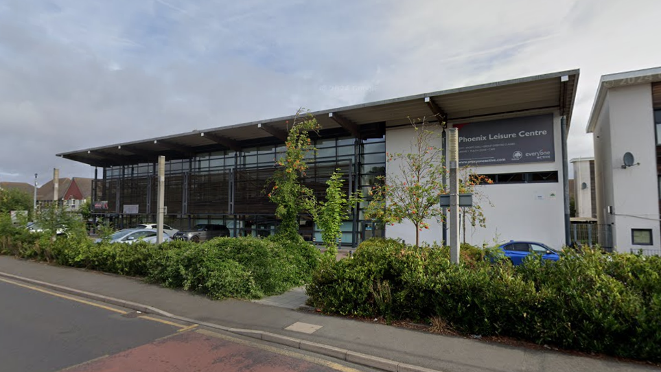 General view of the Phoenix Leisure Centre, a modern glass and concrete building which sits behind hedging and trees along a main road