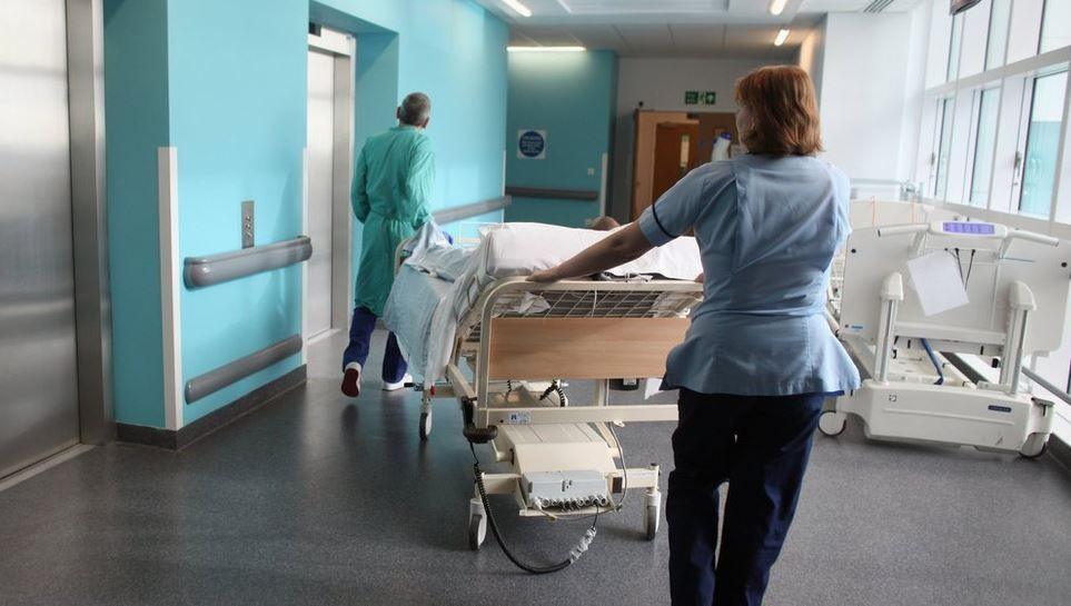 A patient being moved in a hospital bed along a blue corridor by two hospital workers.