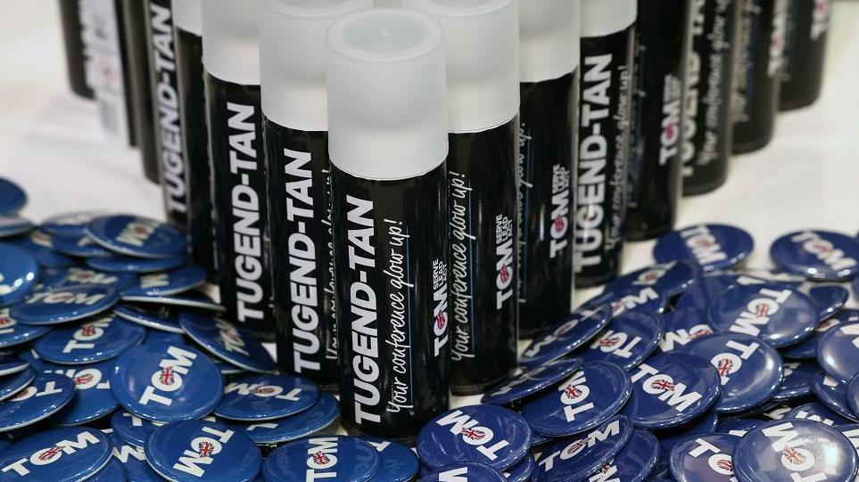 Cans of promotional Tugend-tan lined up on a bed of Tom Tugendhat badges at the Tory conference in Birmingham