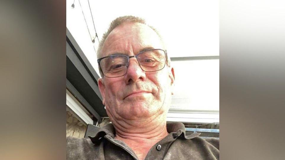 Martin is wearing a grey top and glasses and has short brown hair in this selfie image.