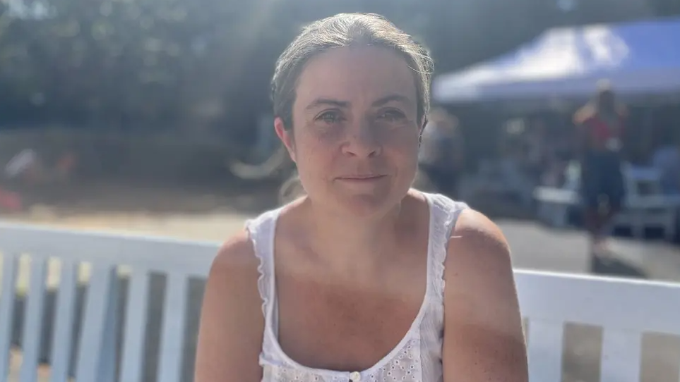 Louise Ravenscroft, wearing a sleeveless white top and smiling for the camera. She is sitting outside on a white wooden bench.