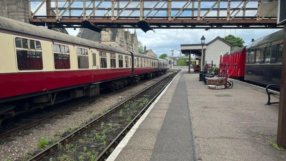 Nene Valley railway station. An old fashioned train with carriages painted red and cream, and an old fashioned station house canopy and an overhead footbridge.