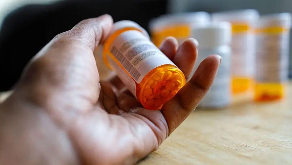 A person's hand is holding an orange plastic bottle with white pills inside