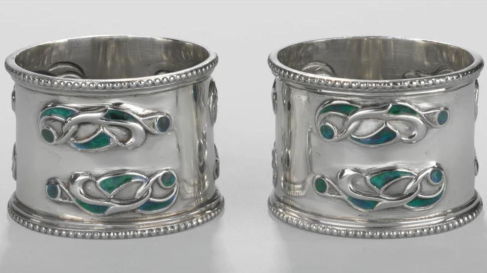 A pair of silver napkin rings embossed with a Celtic interlocking design in green and turquoise.