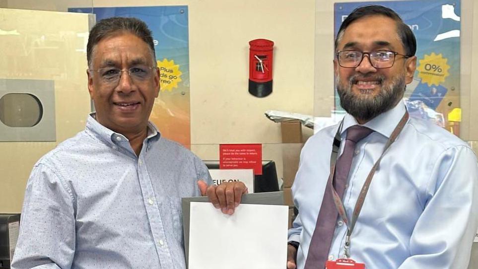 Chani Gill (left) presented with a framed certificate for his long service at Cobham Post Office