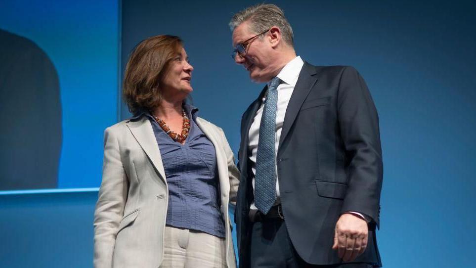 Eluned Morgan stood alongside Sir Keir Starmer at Welsh Labour conference last year. Morgan is wearing a blue top and grey suit, while Sir Keir is wearing a black suit, a blue tie, a white shirt and glasses.