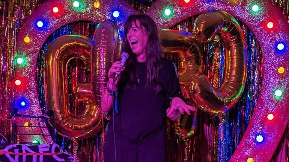 Paula on a stage holding a microphone.
