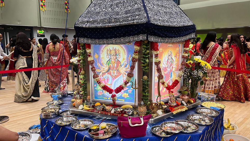 Silver plates of offerings of fruit and nuts left at the shrine to the nine different goddesses with women in colourful sarees in the background